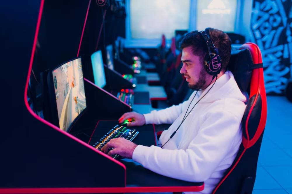 A gamer wearing headphones focuses intently on a colorful computer screen, surrounded by sleek gaming setups with ambient lighting.