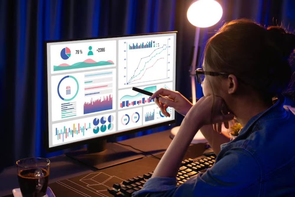 A gamer analyzes colorful data visualizations on a computer screen, with a cup of coffee on the desk in a dimly lit room.