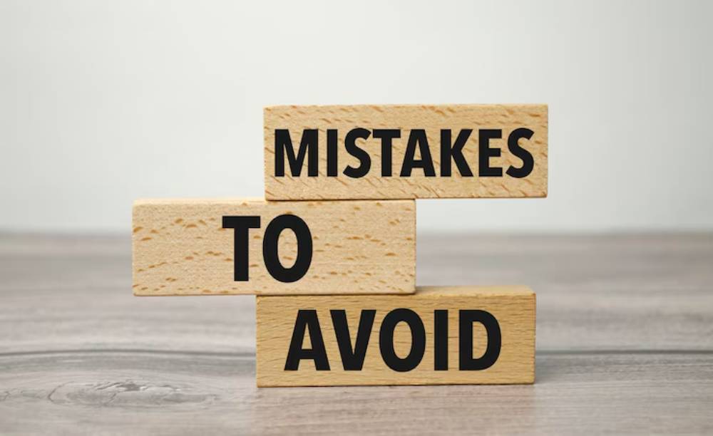 Wooden blocks stacked to read 'MISTAKES TO AVOID' on a gray wooden surface, emphasizing caution and guidance.