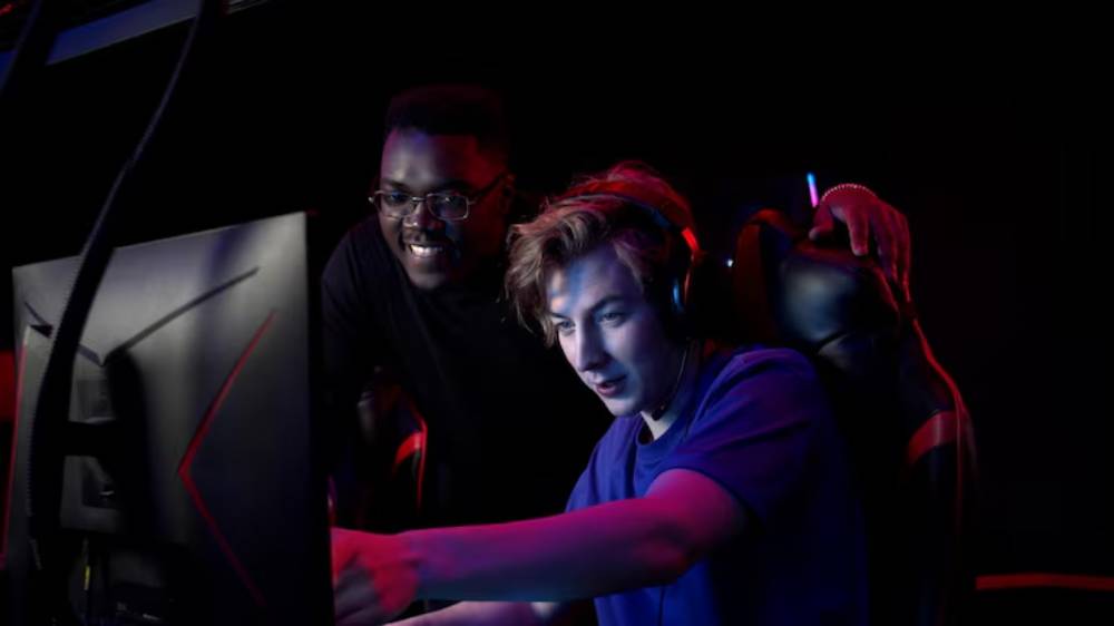Two gamers are intensely focused on a computer screen, surrounded by a dark, colorful gaming setup.