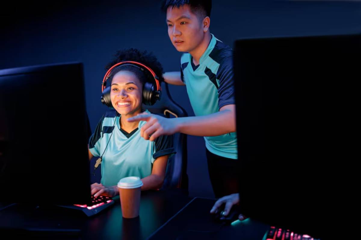 Gamer and their coach collabarate at a gaming setup, with monitors and a coffee cup on the desk.