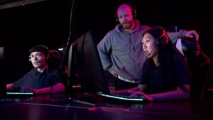 Two gamers are engaged in a gaming session at a sleek and their coach is stand nearby.