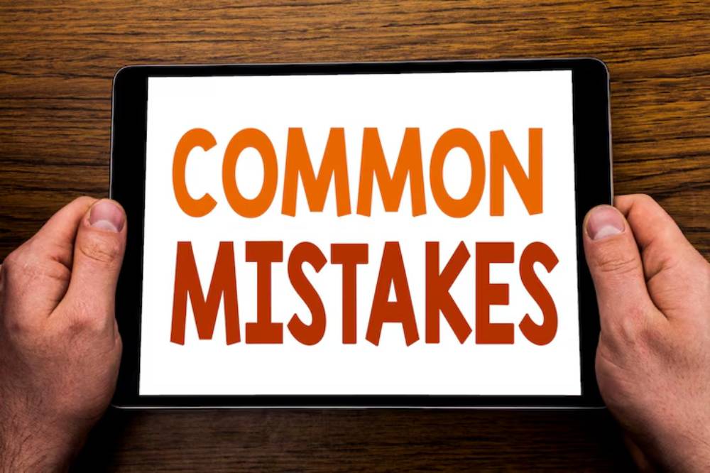 A person holds a tablet displaying the bold text 'COMMON MISTAKES' against a white background, set on a wooden table.