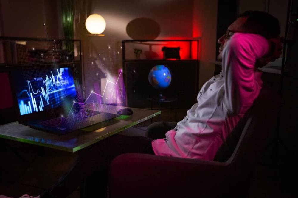 A person in a white shirt sits on a couch, gazing at a laptop displaying colorful data visualizations and glowing holographic graphs.