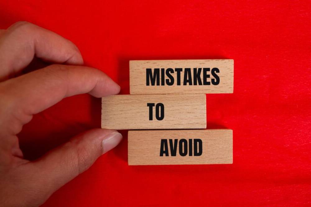 A hand holds wooden blocks displaying the text 'MISTAKES TO AVOID' against a bright red background.