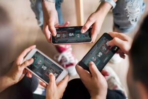 Four hands holding smartphones displaying a competitive mobile game screen showing "VS" and character selections.