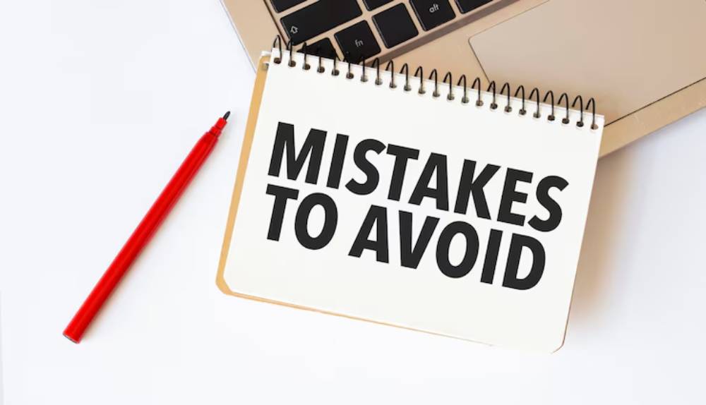 A notepad with- 'MISTAKES TO AVOID' written in bold black letters, next to a red pen and a laptop keyboard.