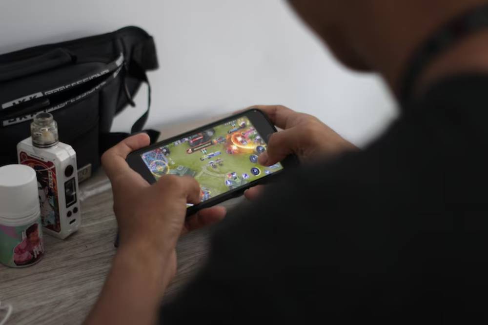 A person playing a mobile game on their phone, with a vape device and container near them.