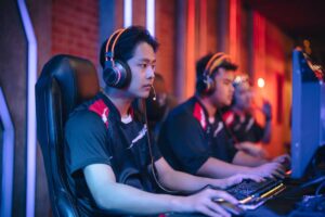 Three gamers in matching black shirts and headphones focus intently on their screens, illuminated by colorful ambient lighting.