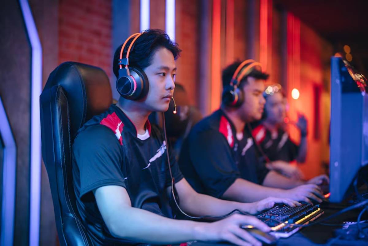 Three gamers in matching black shirts and headphones focus intently on their screens, illuminated by colorful ambient lighting.