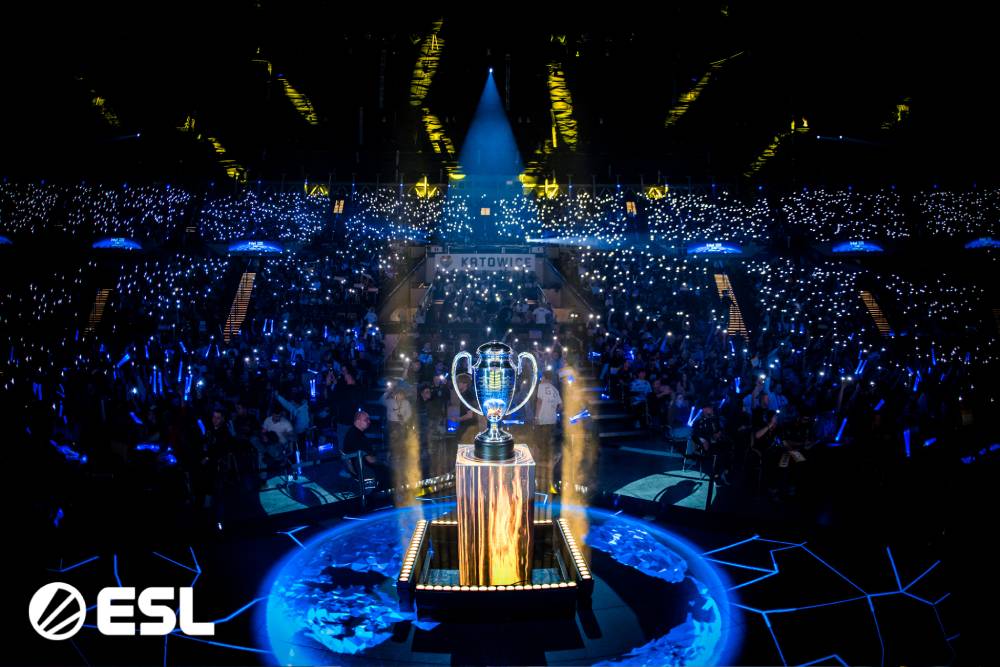 A festive esports arena illuminated by fans' lights, centered around a trophy onstage, highlighting the excitement of the competition.