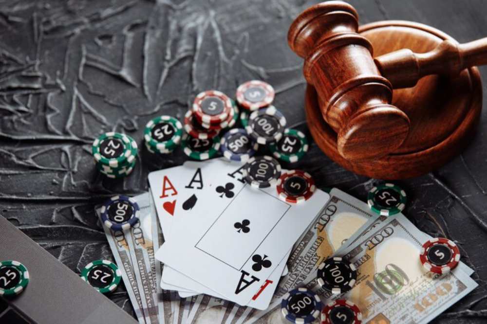 A gavel rests next to poker chips, playing cards, and bundles of cash, symbolizing gambling and legal issues.