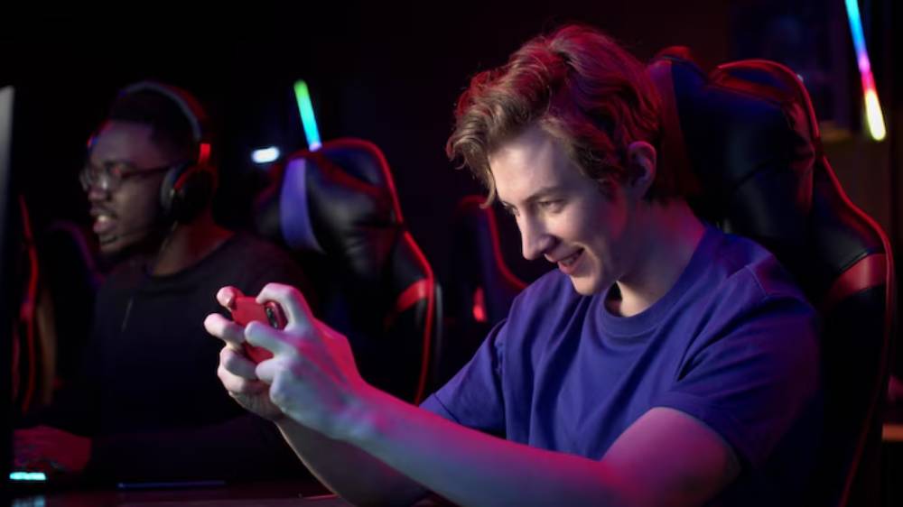 A young gamer in a blue shirt intently plays on a mobile device, surrounded by colorful LED lights in a dark gaming setting.