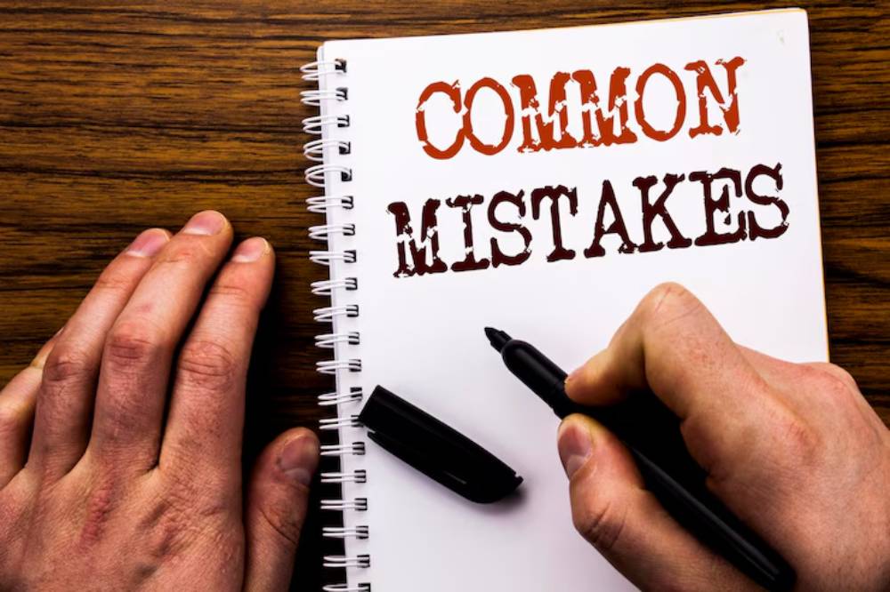 A person’s hand holds a pen over a notebook titled-Common Mistakes, with a wooden table surface visible beneath.