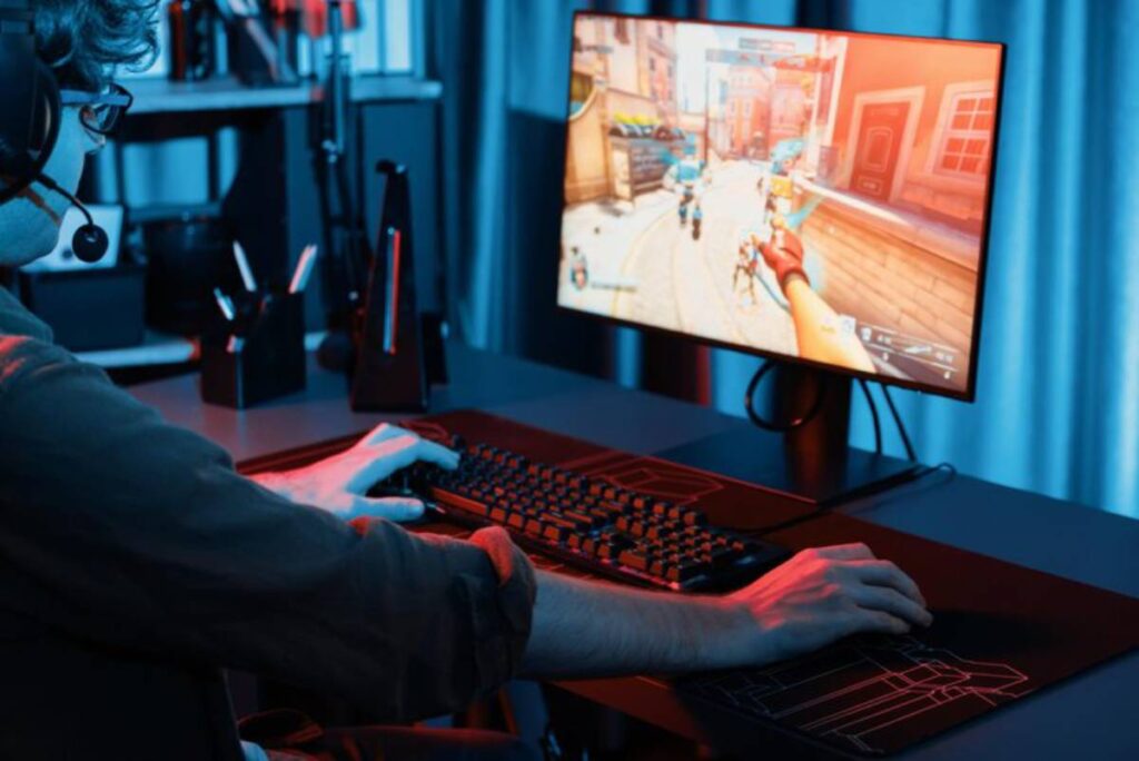 A gamer with a headset plays on a desktop, focused on an action-packed video game displayed on a vibrant monitor.