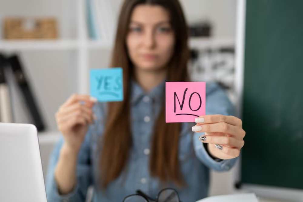 A person holds two sticky notes, one blue with 'YES' and one pink with 'NO,' against a blurred office background.