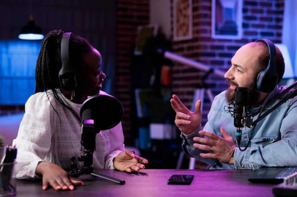 A podcast recording session featuring one gamer and one influencer engaged in conversation at a stylish table with microphones and headphones.