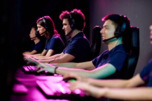 A group of gamers seated at computers, wearing headsets, engaged in an intense gaming session with colorful backlighting.