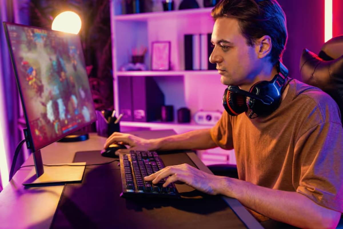 A gamer in a cozy room, focused on an action-packed game on the monitor, wearing headphones and typing on a sleek keyboard.
