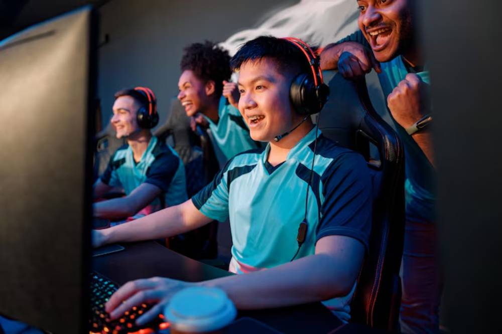 A group of focused gamers in matching teal jerseys and headsets competes at a gaming station, illuminated by colorful lights. 