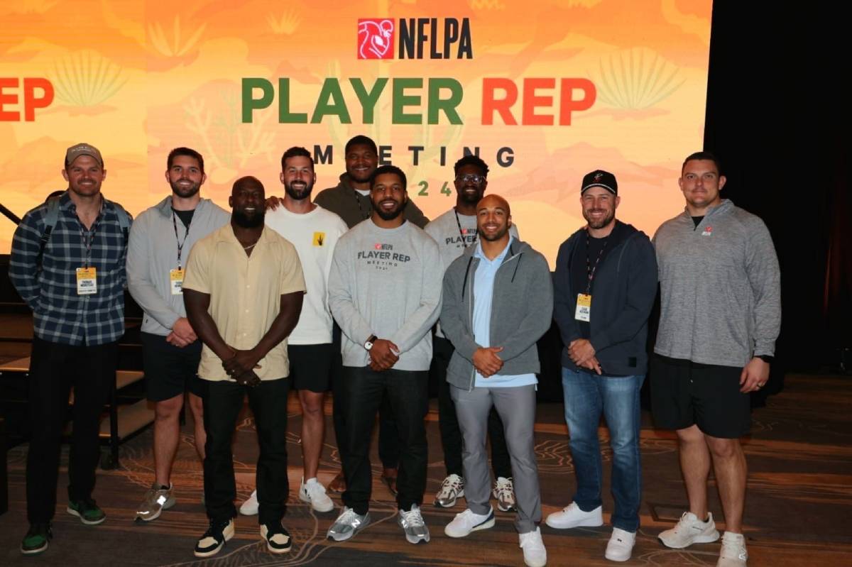 A group of NFL players stands in front of a brightly colored banner that reads 