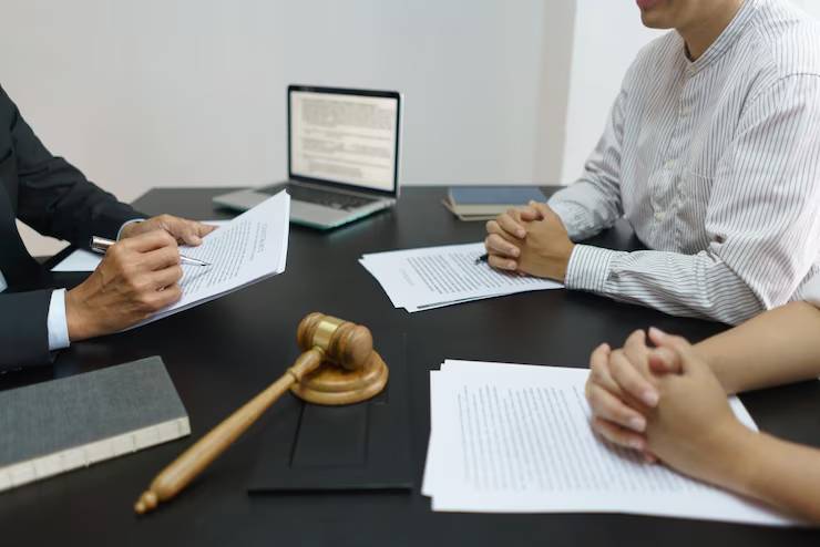 A lawyer discusses legal documents with clients at a table, featuring a laptop and a gavel nearby.